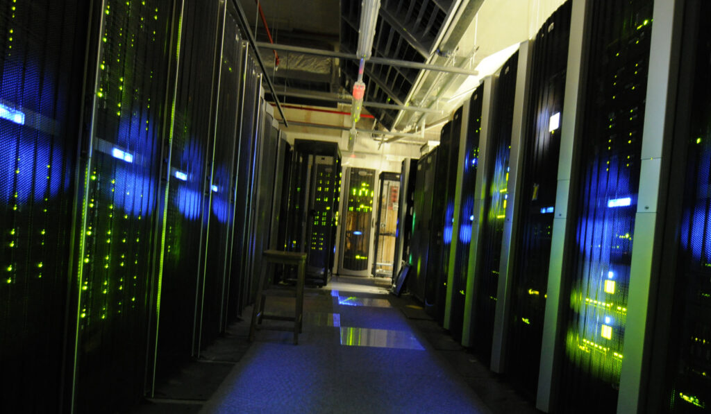 Aisle between black server cabinets with illuminated status lights and overhead cabling.