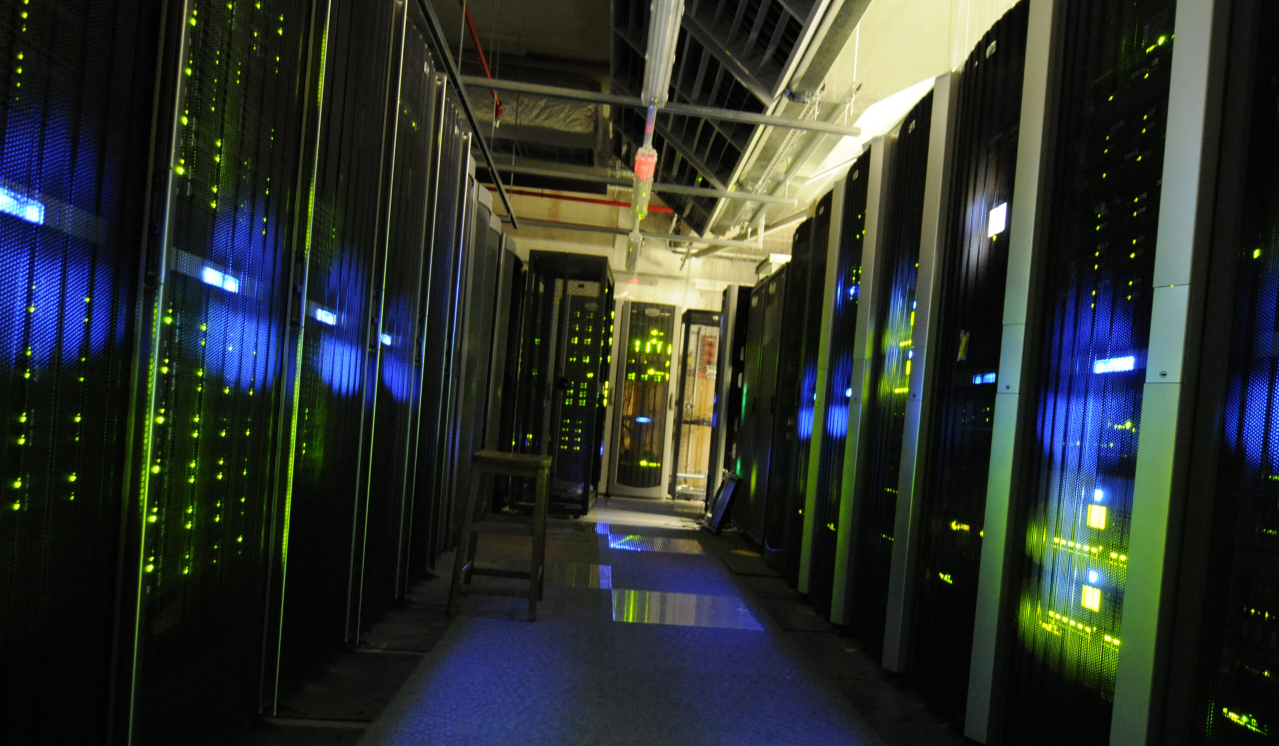 Aisle between black server cabinets with illuminated status lights and overhead cabling.